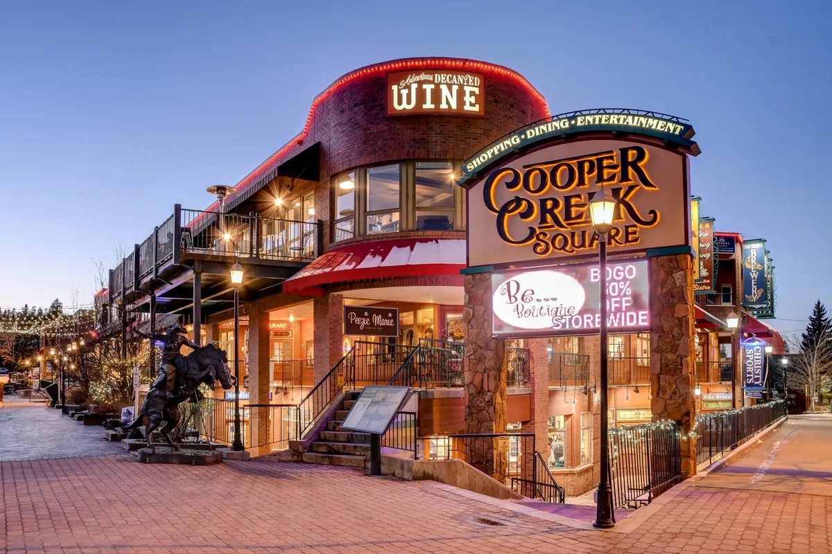 An exterior shot of Cooper Creek Square, with visible signage, an inviting outdoor seating area, and a festive atmosphere ideal for shopping, dining, and gathering. A horse statue adds unique local charm.