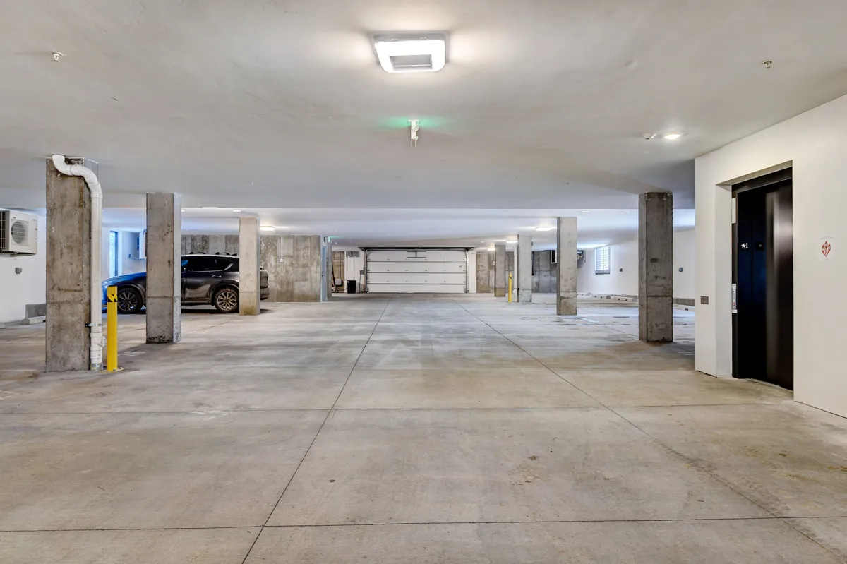 An interior view of the underground parking garage, featuring clearly marked parking spaces, concrete pillars, and an elevator for direct building access.