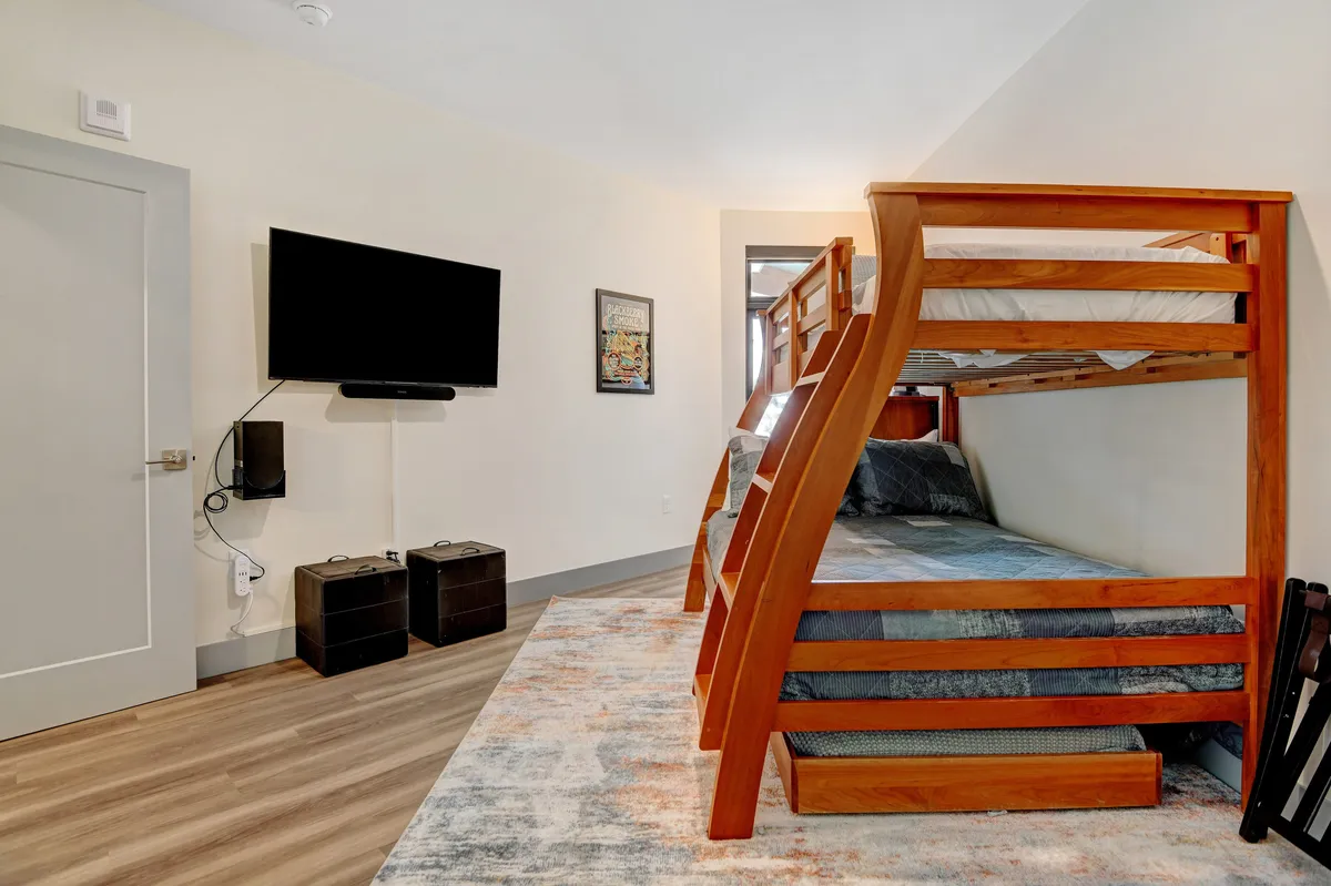 A playful and comfortable bunk room equipped with a twin-over-full bunk bed, cozy bedding, a rug for play, and a wall-mounted smart TV. The room feels bright and family-friendly, perfect for children and guests to relax, play games, or enjoy movie nights.