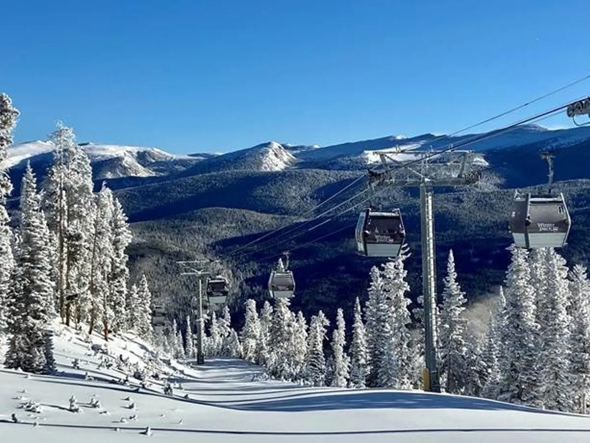 A sweeping winter scene featuring ski lift gondolas gliding over snow-covered slopes with distant mountains and dense pine trees. The image conveys active ski and snowboard adventures in the heart of the Rockies.