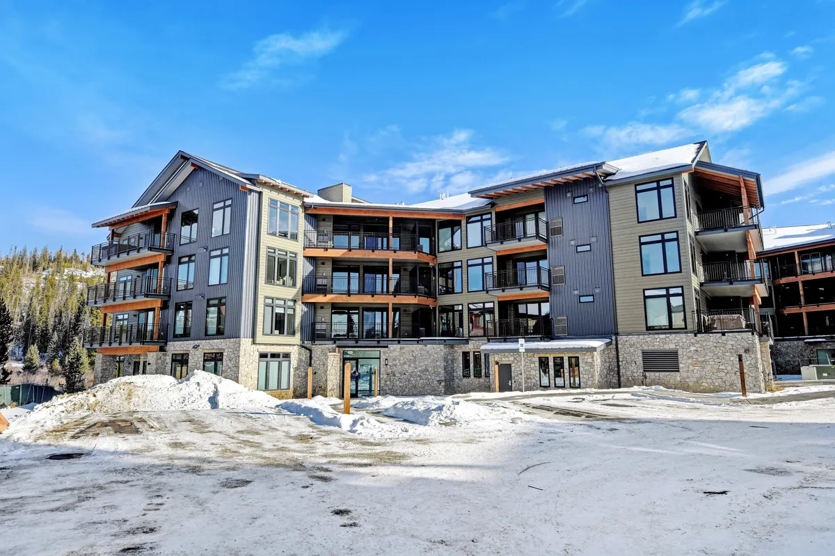 This exterior image highlights the property's striking modern architecture, surrounded by snow and featuring large windows and inviting balconies. The snow-covered ground and the building's contemporary lines evoke a sense of luxury and exclusivity, while the views suggest proximity to mountain adventure and ski activities.