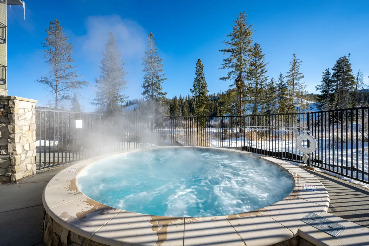 A tranquil scene of a community hot tub nestled among snow-covered trees, inviting guests to relax and unwind in nature after a day of mountain activities.